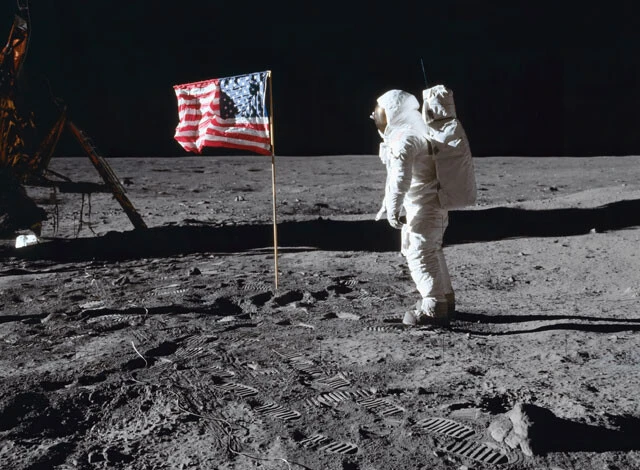 アポロ11号のミッションで、月面で宇宙飛行士がアメリカ国旗の横に立っている画像